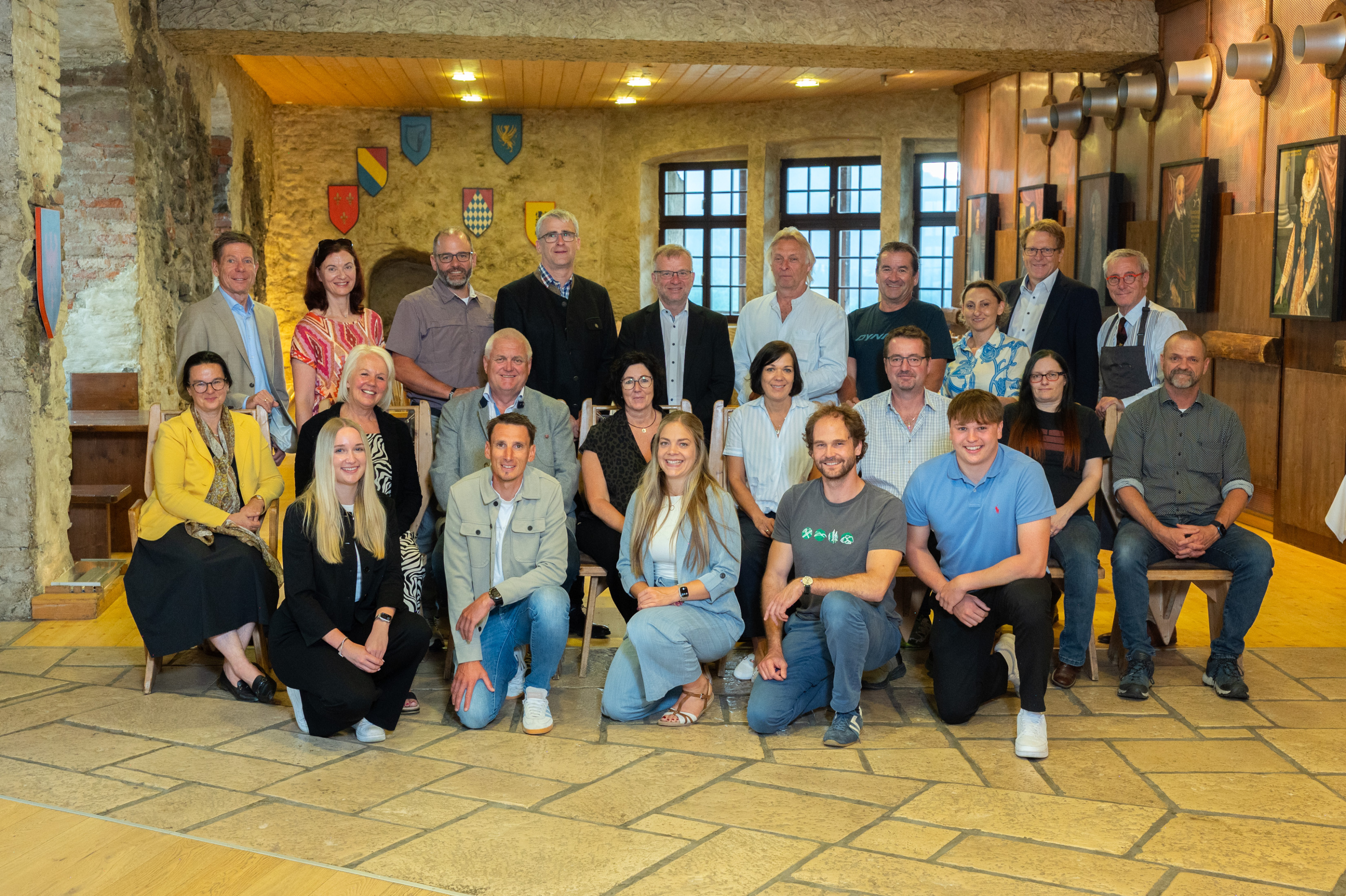 Gruppenfoto von ca. 20 Vertretern der ausgezeichneten Betriebe in einem mittelalterlich anmutenden Raum mit steinernen Wänden und Boden.